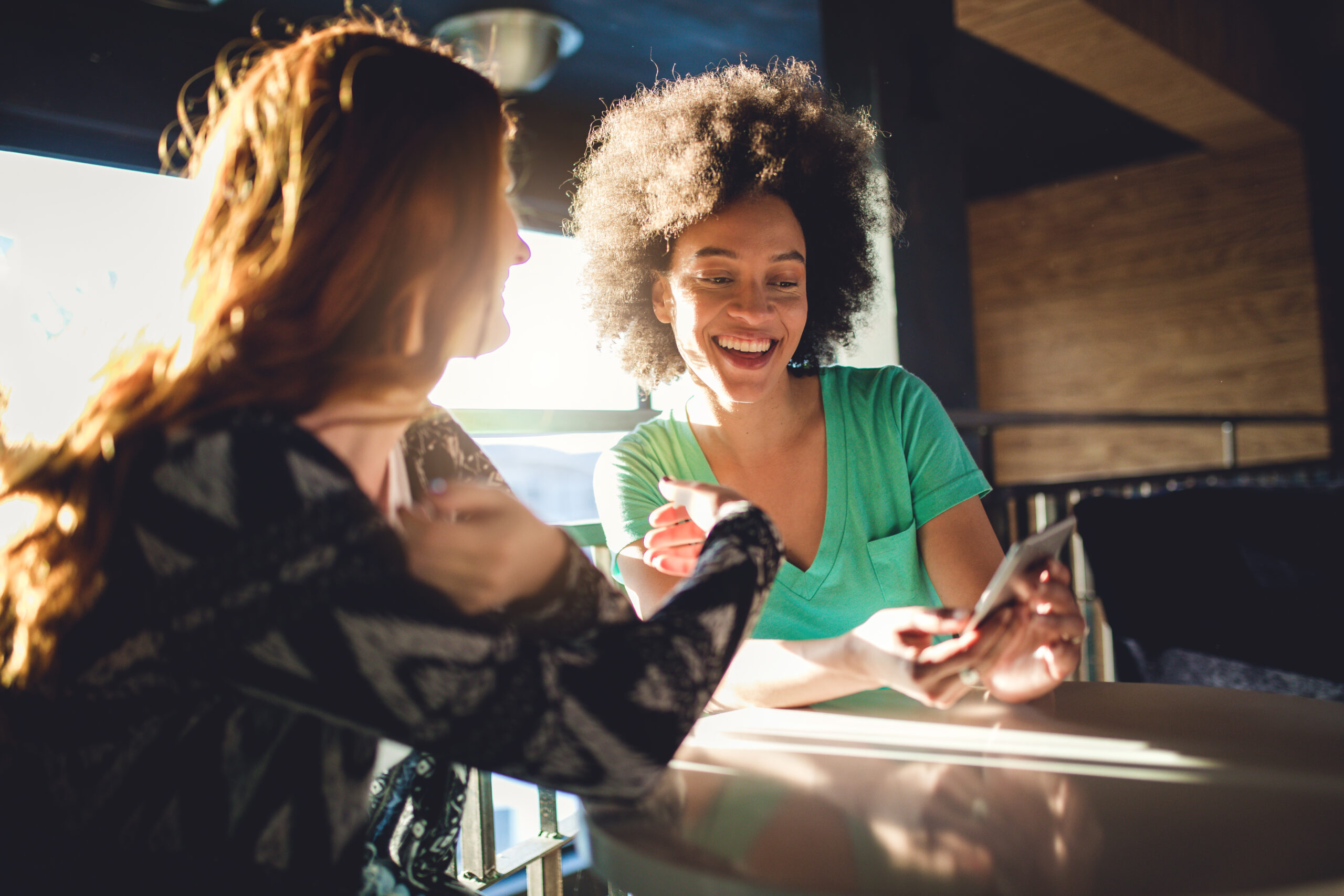 Two friends looking at a mobile phone while sitting in a cafe and smiling